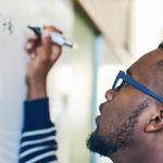 Cropped shot of a young man writing on a whiteboard in a classroom