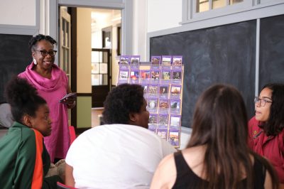 Female teacher in pink blouse fostering classroom culture by instructing students joyfully and using visual learning tools