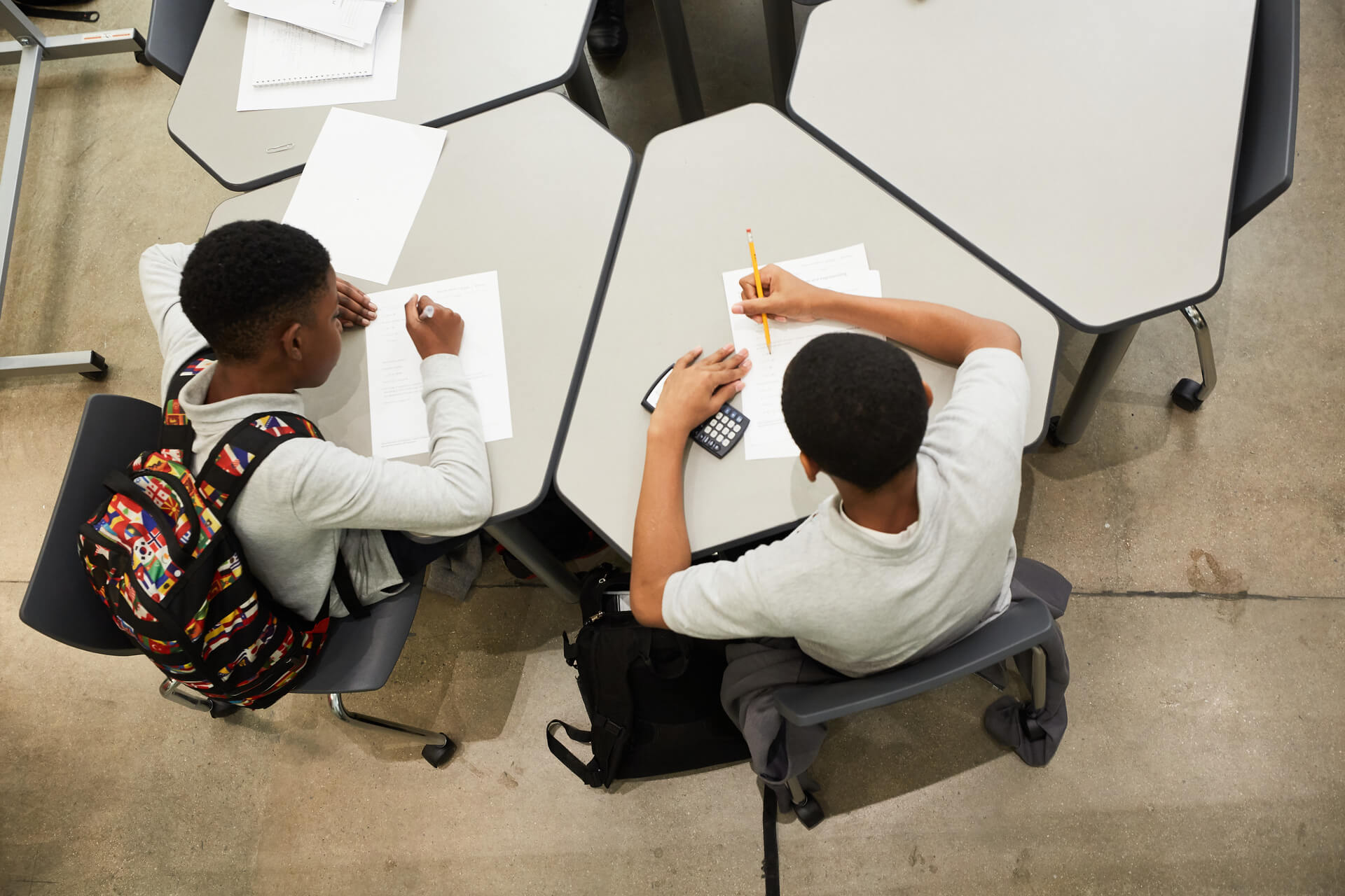 Bird's-eye view of two male students sitting at desks next to each other and writing on pieces of paper