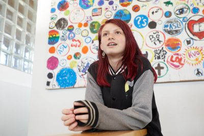 Young female student with red hair seated in a classroom in front of a colorful painting learning about digital badging