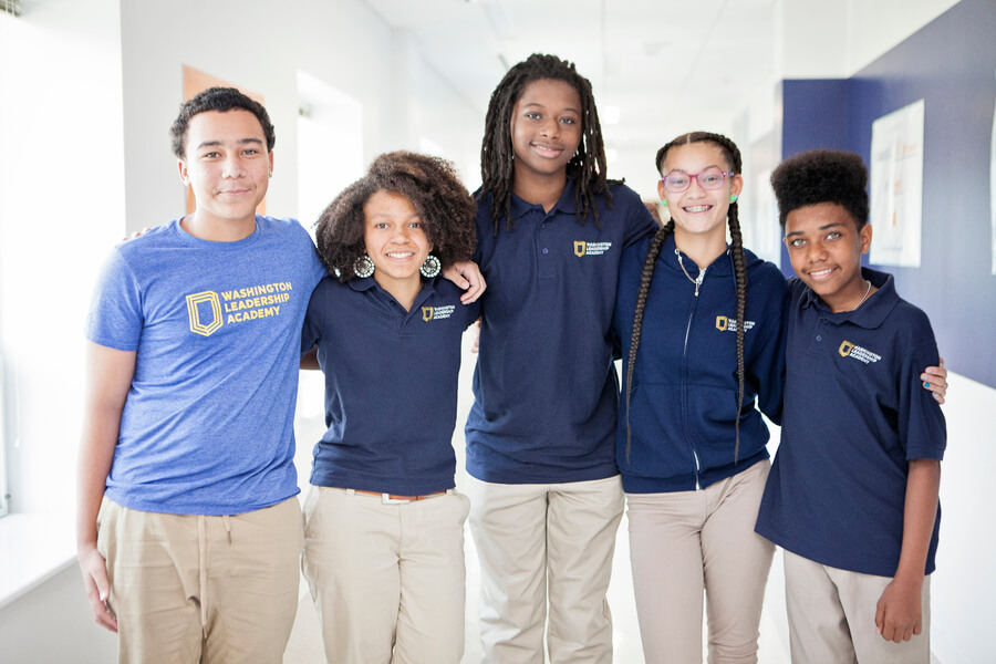 Five students at Washington Leadership Academy wearing school uniforms and smiling with their arms around each other