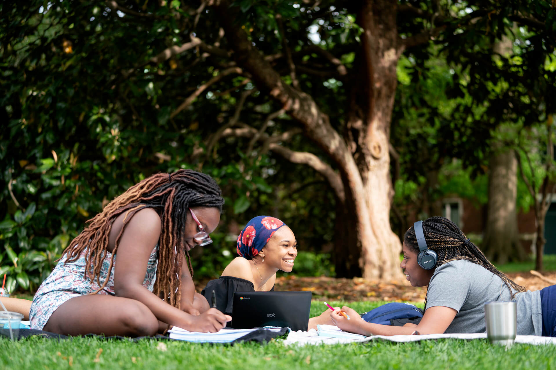Three female students sitting in a grassy park discussing their transition from high school to college