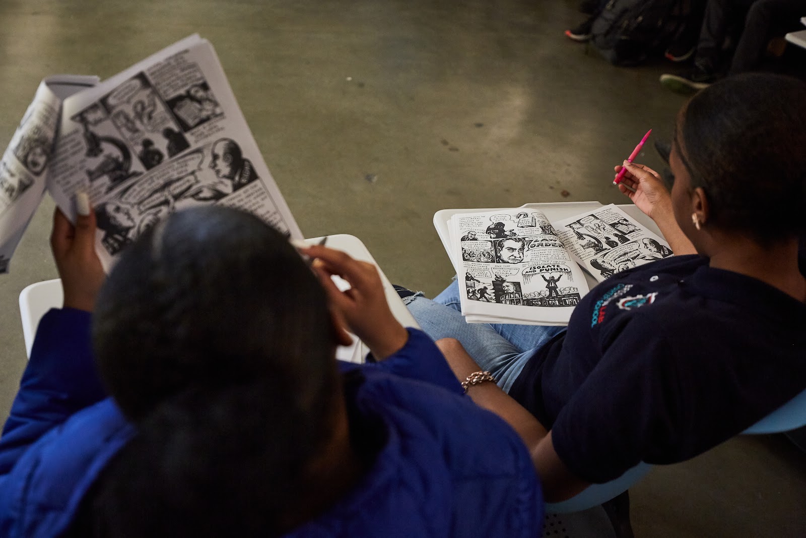 Two students reading a graphic novel text take notes together in a classroom